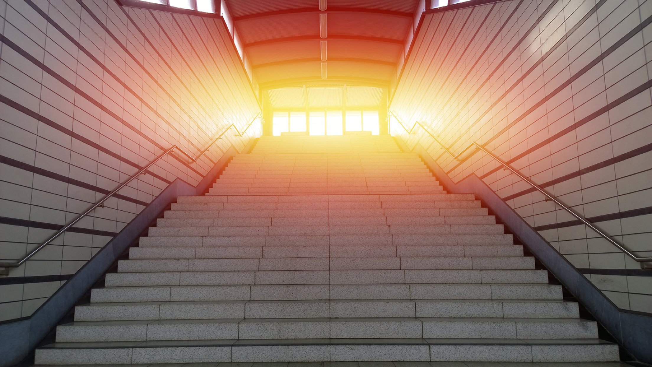 En lång trappa leder upp mot ett starkt ljus genom glasdörrar. Bilden symboliserar att det finns steg att ta – så här kan du agera när du fått ett inkassokrav.